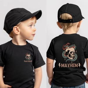 以下が含まれることがあります： 黒のTシャツ。背面には骸骨とヘビのグラフィック、前面には小さな骸骨のグラフィックがプリントされています。シャツには「MAYHEM」の文字がプリントされています。シャツは、黒い野球帽をかぶった子供が着用しています。