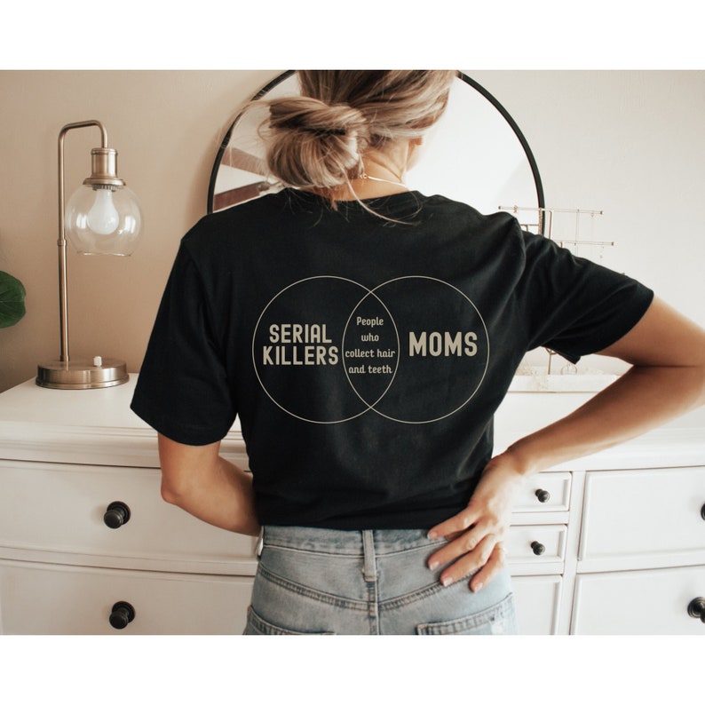 Puede incluir: Una camiseta negra con un gr&aacute;fico de diagrama de Venn que dice "Asesinos en serie" y "Mam&aacute;s" con la secci&oacute;n superpuesta que dice "Personas que recolectan cabello y dientes."