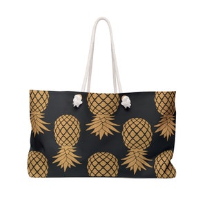 Puede incluir: Una bolsa de lona negra con asas de cuerda blanca y un patrón de piña dorada.