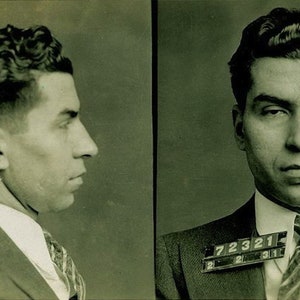 May include: A black and white mugshot of a man with dark hair and a suit. The mugshot has two photos, one with the man looking straight ahead and the other with the man looking to the side. The man is wearing a suit jacket and tie. The mugshot has a number tag on the jacket that reads "72321".