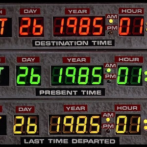 May include: A digital clock display with three rows of information. The top row shows "OCT 26 1985 01:21 PM" and is labelled "DESTINATION TIME". The middle row shows "OCT 26 1985 01:22 PM" and is labelled "PRESENT TIME". The bottom row shows "OCT 26 1985 00:20 PM" and is labelled "LAST TIME DEPARTED".