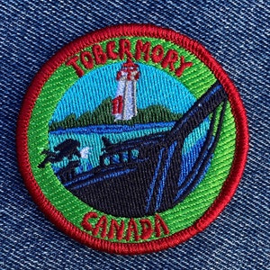 Può includere: Una toppa ricamata verde, rossa e blu con le parole "Tobermory Canada" e un design di faro e barca.