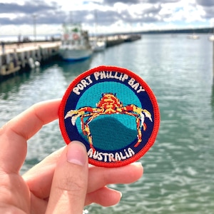 May include: A red, white, and blue embroidered patch with a crab on a blue background. The text "Port Phillip Bay Australia" is on the patch.