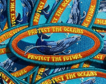 May include: Embroidered patches with a whale design. The patches are oval-shaped with a blue background and an orange border. Text on the patches reads "PROTECT THE OCEANS" and "PROTECT THE FUTURE". The whale is depicted in shades of blue.
