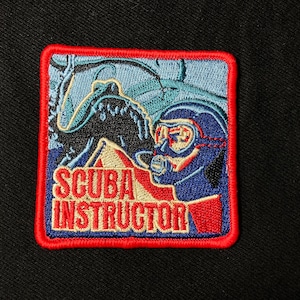 May include: An embroidered patch featuring a scuba diver and the text "SCUBA INSTRUCTOR" in red, white and blue.