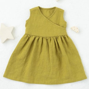 以下が含まれることがあります： マスタードイエローのリネンワンピース。ラップスタイルのボディスとギャザーの入ったスカート。ノースリーブで、シンプルでエレガントなデザインです。