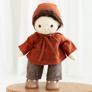 May include: A brown fabric doll with a brown hat, brown shirt, and striped pants. The doll has a white face with brown eyes and a brown mouth.