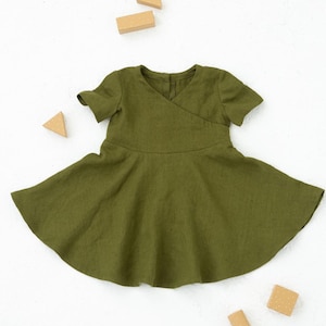 May include: A green linen dress with a wrap-style bodice and short sleeves. The dress has a flared skirt and is photographed against a white background.