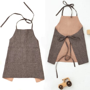 May include: A brown and white striped linen apron with a large pocket in the front. The apron has adjustable straps that tie at the back.
