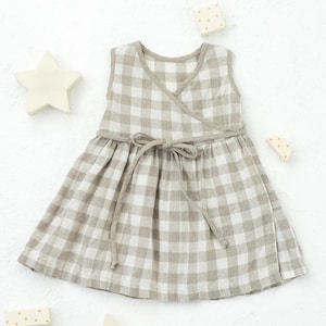 May include: A sleeveless gingham dress with a wrap-style bodice and a tie at the waist. The dress is made of a light brown and white gingham fabric.
