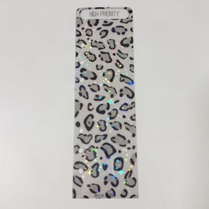 Puede incluir: Un inserto de planificador rectangular con un diseño de estampado de leopardo y las palabras "HIGH PRIORITY" en la parte superior. El inserto tiene un fondo gris claro con manchas negras y plateadas. El inserto tiene varios agujeros para encuadernar.