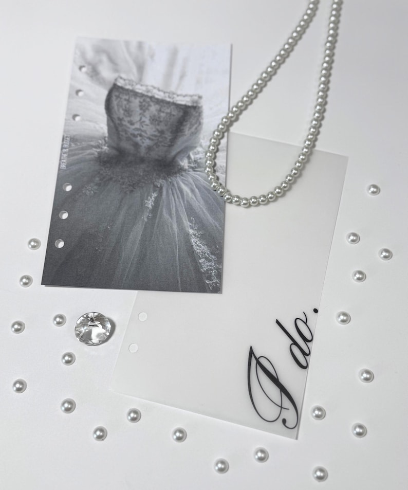 Puede incluir: Una tarjeta blanca con las palabras "I do" escritas en cursiva negra. La tarjeta est&aacute; rodeada de cuentas de perlas blancas y una foto en blanco y negro de un vestido de novia.