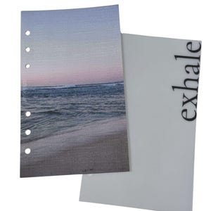 May include: Two-piece planner inserts. One insert features a beach scene with a blue and pink sky, and the other is white with the word "exhale" in black. The beach scene insert has six holes for binding.