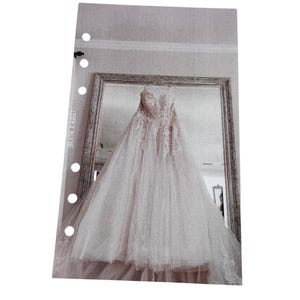 Puede incluir: Un vestido de novia blanco con detalles de encaje cuelga en una habitaci&oacute;n con un espejo. El vestido tiene un escote de coraz&oacute;n y una falda completa.