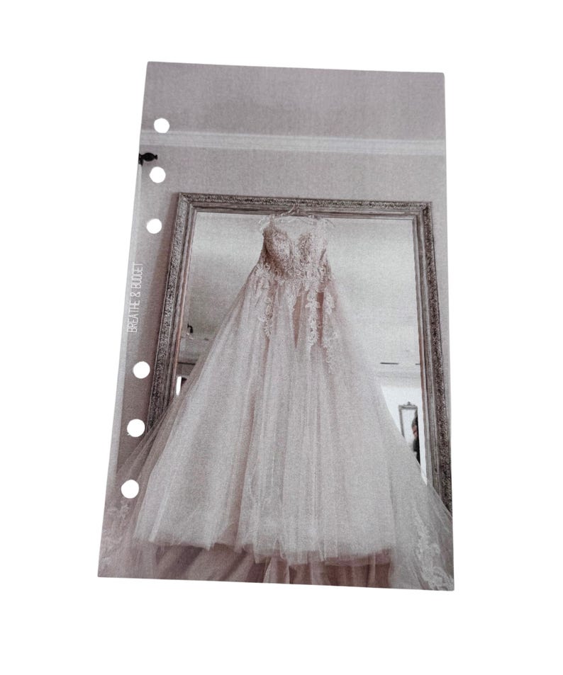 Puede incluir: Un vestido de novia blanco con detalles de encaje cuelga en una habitaci&oacute;n con un espejo. El vestido tiene un escote de coraz&oacute;n y una falda completa.