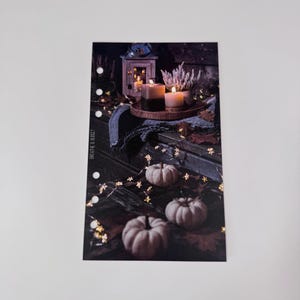 Puede incluir: Insert de planificador con una escena oto&ntilde;al. La imagen muestra velas encendidas, una linterna y peque&ntilde;as calabazas sobre una superficie de madera, con luces de cadena y hojas de oto&ntilde;o. El texto "BREATHE & BUDGET" es visible.