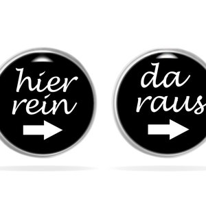 Peut inclure: Deux boutons ronds noirs avec du texte blanc et des flèches. Le bouton de gauche dit "hier rein" avec une flèche pointant vers la droite. Le bouton de droite dit "da raus" avec une flèche pointant vers la droite.