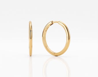 May include: A pair of gold-toned hoop earrings with a smooth, polished finish. One earring is shown from the side, while the other is angled to reveal the circular shape and the small 925 hallmark stamped on the metal surface of the hoop.