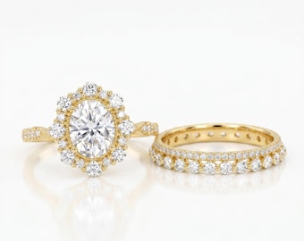 May include: A gold engagement ring with an oval-cut center stone surrounded by a halo of smaller stones. A matching gold band with a row of small stones is next to the engagement ring. The rings are set against a white background.