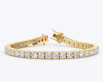 May include: A gold tennis bracelet with a row of round, clear gemstones. The bracelet is open, showing the clasp and the detailed link design. The background is plain white.