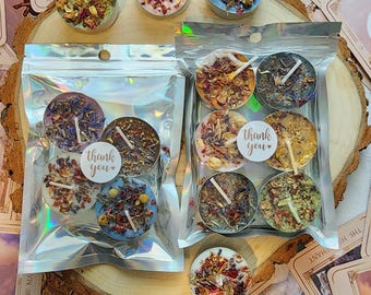 May include: Assortment of small, round candles in various colors, decorated with dried flowers and herbs. Some candles are packaged in clear, iridescent bags. The image includes tarot cards and candles with "thank you" stickers.