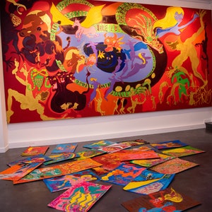 May include: A large, colourful painting depicting a fantastical scene with multiple figures and creatures. The painting is set against a red background and features a variety of colours, including yellow, green, blue, and purple. The painting is displayed on a wall in a gallery setting, with several smaller, colourful paintings scattered on the floor in front of it.