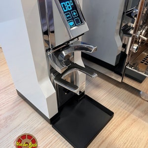 Op de afbeelding: Een witte koffiebonenmaler met een digitaal display dat "08.0" en het woord "LIBRA" op de voorkant laat zien. De maler heeft een zwarte opvangbak en een zilveren handvat.