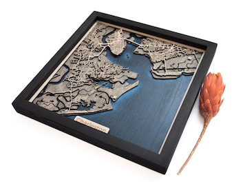 May include: A wooden map of Charleston, South Carolina, with a black frame and a blue-green water feature. The map is raised and has a 3D effect.