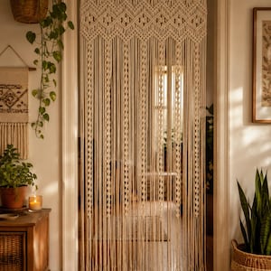 May include: A cream-colored macrame door curtain featuring an intricate woven diamond pattern at the top, transitioning into long, vertical hanging cords with alternating twisted knot details that extend down to the floor in a fringe design.