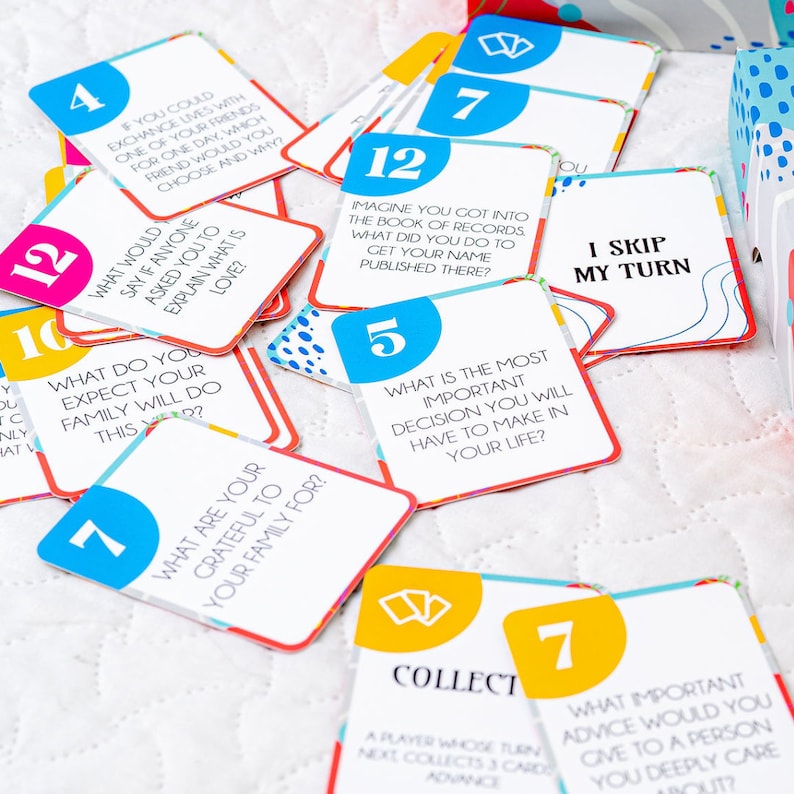 Op de afbeelding: Een set kleurrijke spelkaarten met vragen en instructies. De kaarten zijn rood, geel, blauw en wit met zwarte tekst. De kaarten hebben nummers erop, zoals 4, 7, 10, 12 en 5. Sommige van de vragen op de kaarten zijn: "Wat zou je zeggen als iemand je zou vragen om uit te leggen wat liefde is?" en "Wat is de belangrijkste beslissing die je in je leven zult nemen?"