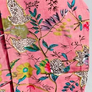 Pu&ograve; includere: Primo piano di un tessuto rosa con un motivo floreale. Il design presenta vari fiori e foglie nelle tonalit&agrave; del verde, blu, giallo e rosso. Il tessuto ha un aspetto morbido e strutturato, suggerendo che potrebbe essere cotone o un materiale simile.