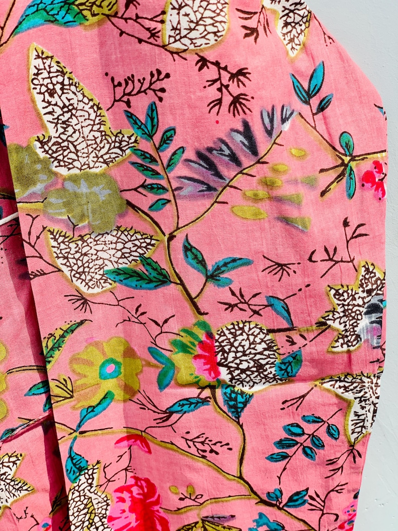 Pu&ograve; includere: Primo piano di un tessuto rosa con un motivo floreale. Il design presenta vari fiori e foglie nelle tonalit&agrave; del verde, blu, giallo e rosso. Il tessuto ha un aspetto morbido e strutturato, suggerendo che potrebbe essere cotone o un materiale simile.