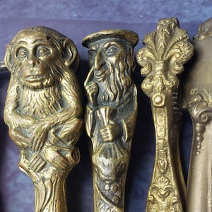 May include: A collection of five metal nutcrackers arranged side by side. The set includes a silver-toned horse figure, a brass monkey, a brass figure of a bearded person, and two ornate brass nutcrackers with intricate decorative patterns.