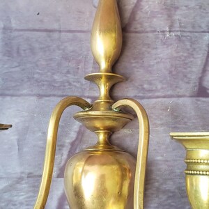 May include: A vintage brass wall sconce with a three-arm design. The sconce features a central, pear-shaped body and curved arms, all in a warm, golden hue. The sconce is approximately 12 inches tall.