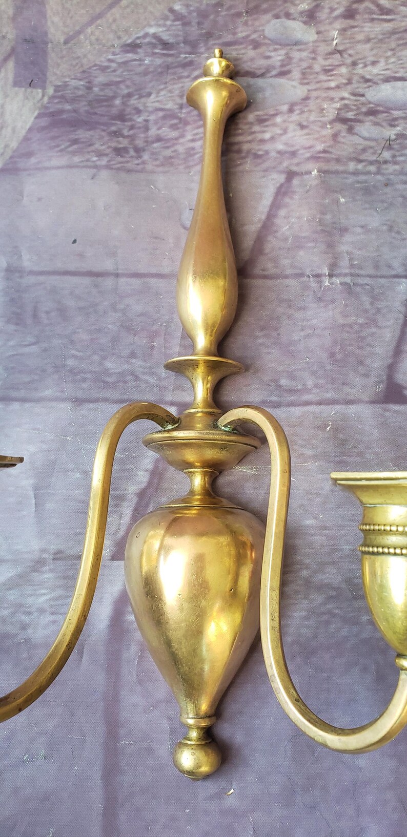 May include: A vintage brass wall sconce with a three-arm design. The sconce features a central, pear-shaped body and curved arms, all in a warm, golden hue. The sconce is approximately 12 inches tall.
