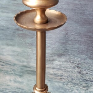 May include: A pair of gold metal candle holders with a decorative design. The candle holders have a round base and a tall, slender stem. The top of the candle holder is a round, open cup.