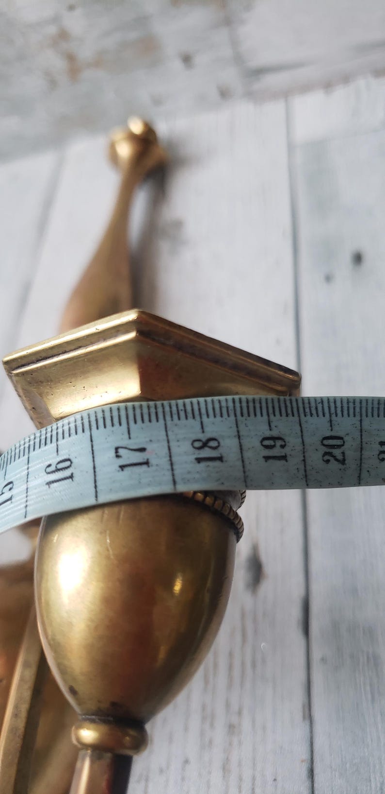 May include: A vintage brass candlestick holder with a square top and a bulbous base. The width of the base is approximately 1.5 inches. The candlestick holder is against a white wooden background.