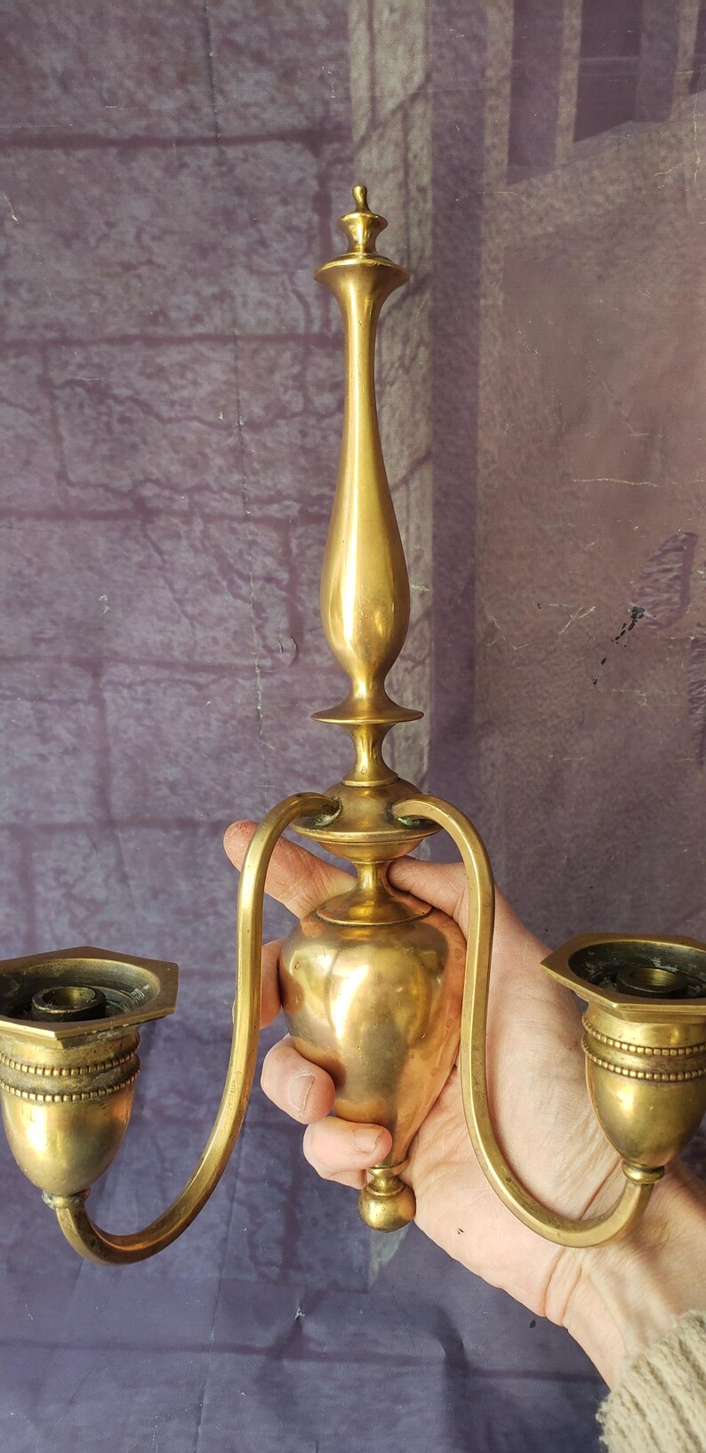 May include: A vintage brass candle holder with two arms and a central stem. The candle holders have a detailed design and are held by curved arms. The brass has a warm, aged patina, suggesting it is an antique.