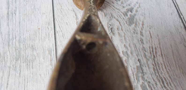 May include: A close-up shot of a dark brown, teardrop-shaped object with a hole. The object appears to be made of wood or a similar material. The background is a light-colored, weathered wooden surface.