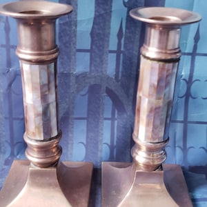 May include: A pair of brass candle holders with a mother of pearl inlay. The candle holders have a square base and a cylindrical body.