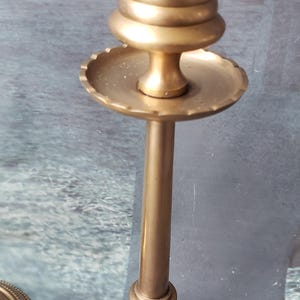 May include: A pair of gold metal candle holders with a decorative design. The candle holders have a round base and a tall, slender stem. The top of the candle holder is a round, open cup.