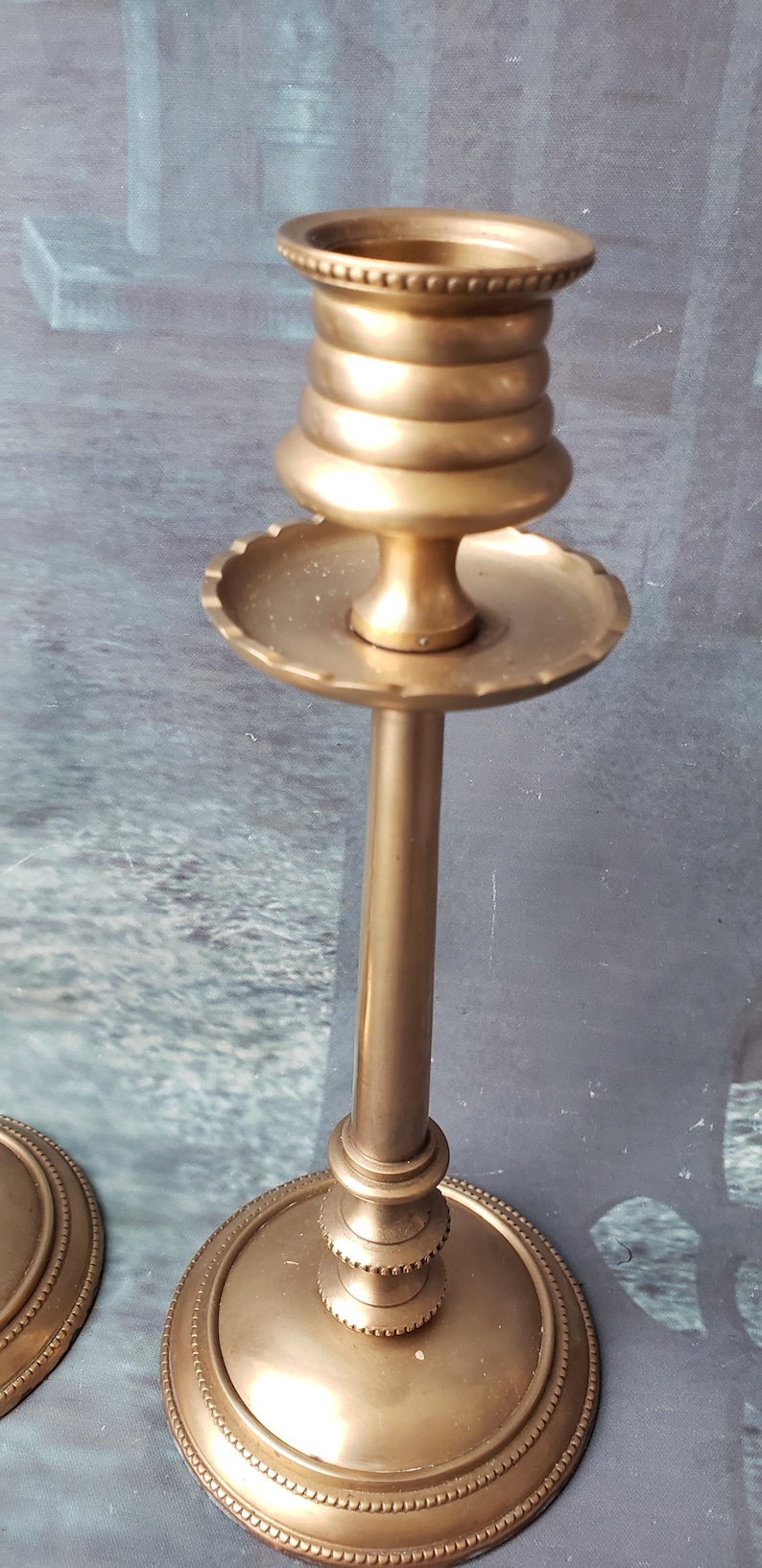 May include: A pair of gold metal candle holders with a decorative design. The candle holders have a round base and a tall, slender stem. The top of the candle holder is a round, open cup.