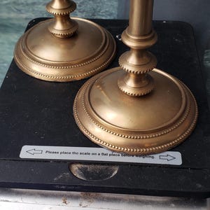 May include: Two gold metal candle holders with a beaded design on the base. The candle holders are on a digital scale that reads 900 grams.