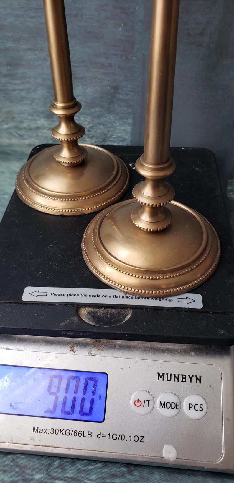 May include: Two gold metal candle holders with a beaded design on the base. The candle holders are on a digital scale that reads 900 grams.