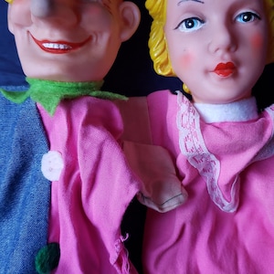 May include: A pair of hand puppets, one with a red hat and a large nose, the other with a purple crown and blonde hair. Both puppets are wearing colourful clothing.