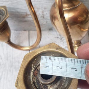 May include: Vintage brass candle holder with a curved arm and hexagonal base. The base measures approximately 1.25 inches across. The candle holder has a tarnished, aged appearance, suggesting it is antique.