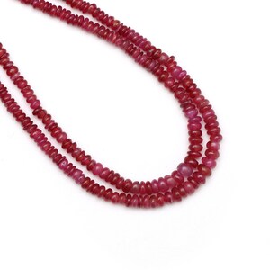 Peut inclure: Un collier de perles de rubis rouges, de forme ronde et lisse. Les perles sont enfilées sur un fil transparent et disposées en double rangée.