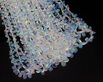 May include: A strand of white opal gemstone beads, each bead is a teardrop shape with iridescent rainbow colors. The beads are strung on a clear thread and are arranged in a cascading pattern.