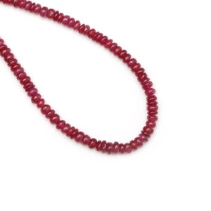 Può includere: Una collana di perle rosso rubino infilate su un filo sottile. Le perle sono rotonde e lisce, e sono tutte della stessa dimensione.