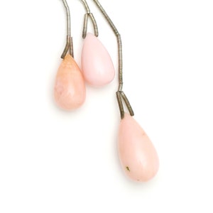 May include: A necklace featuring three teardrop-shaped beads in pink and peach hues. The beads are suspended on thin, silver-coloured wire. The background is plain white.